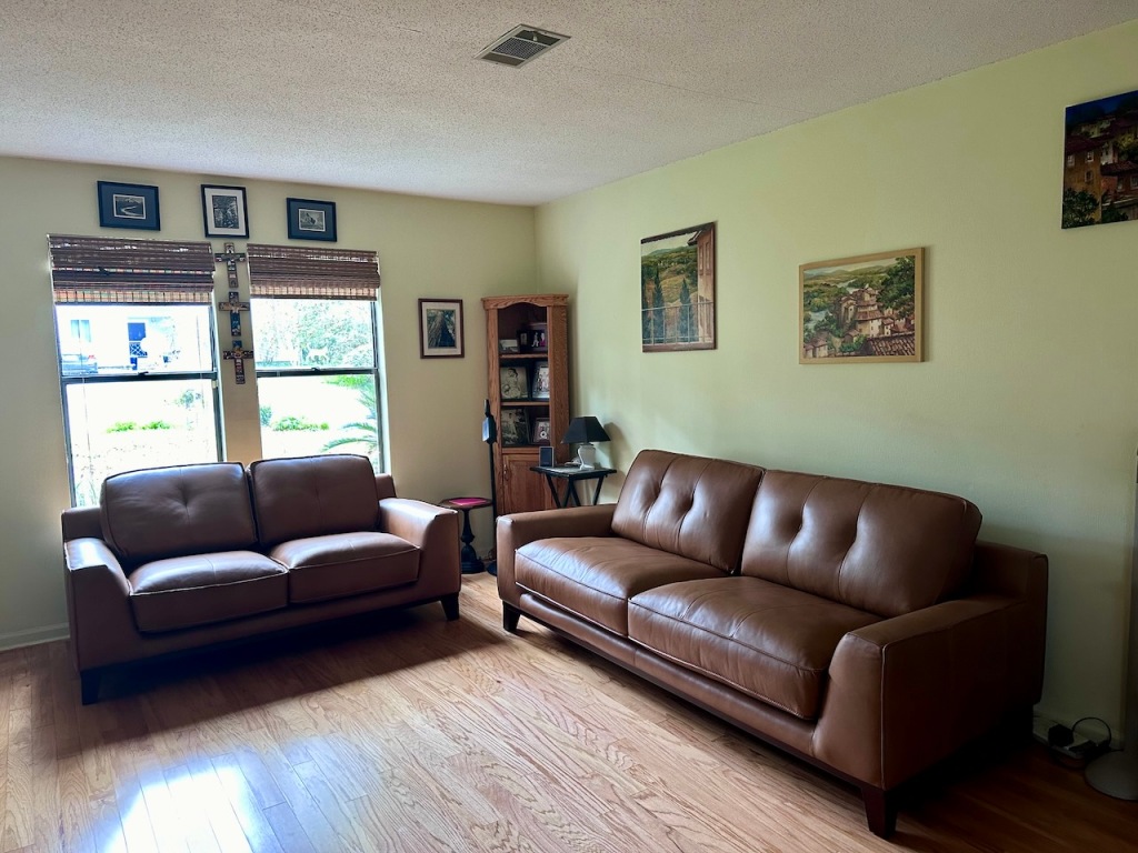 A brown leather loveseat and a brown leather sofa in a living room with bare wood floor.