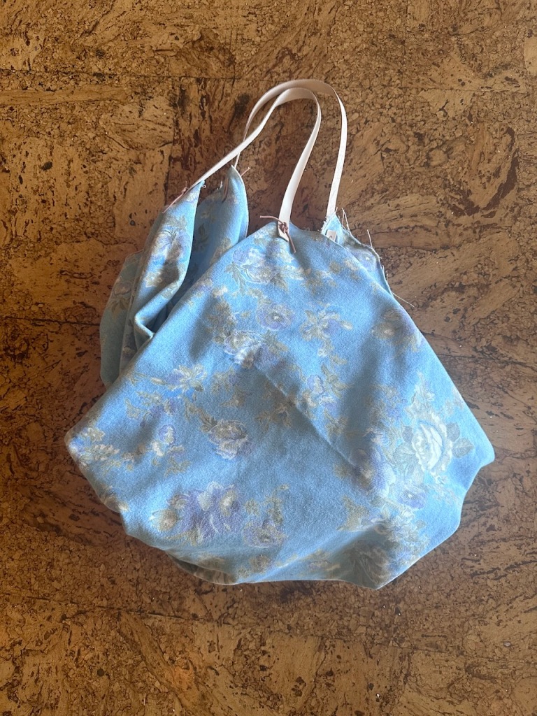 A bag made of light denim fabric with a muted flower pattern and leather straps.
