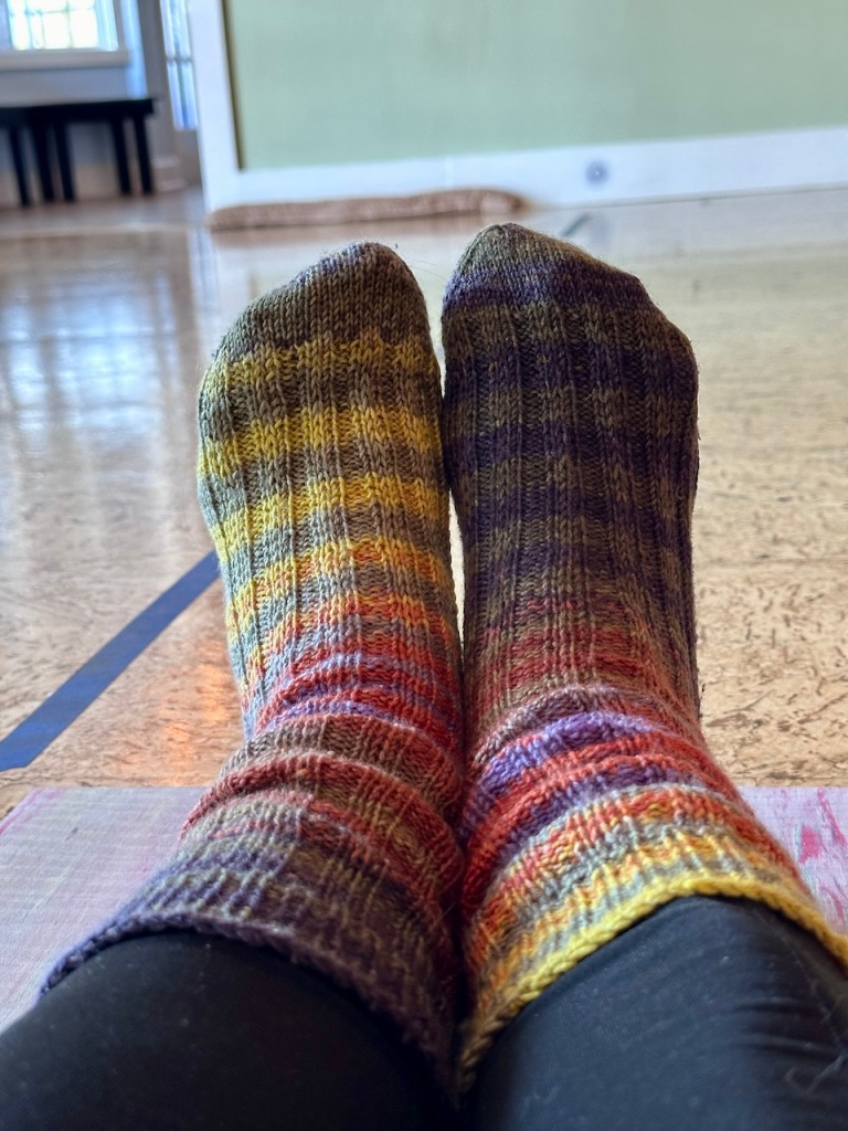 A pair of feet clad in striped socks, colors ranging from yellow to green to red to purple.
