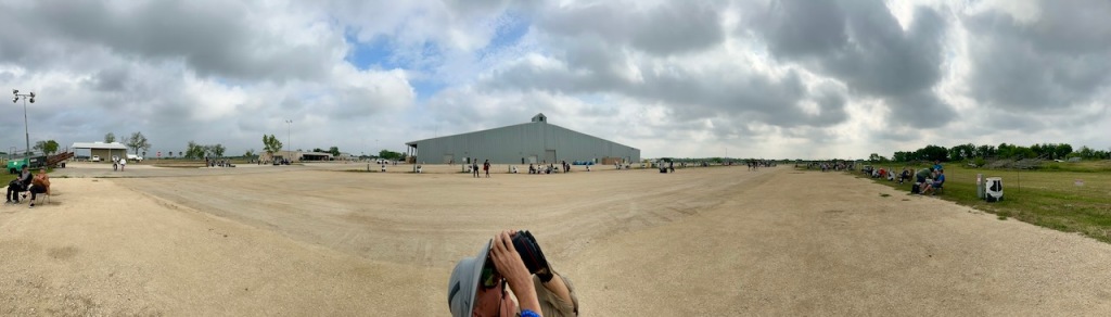 Panoramic of sandy ground, cloudy skies, and a man looking up at the sky with binoculars.